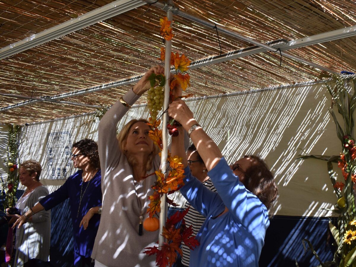 2 women adjust decorations in a sukkah