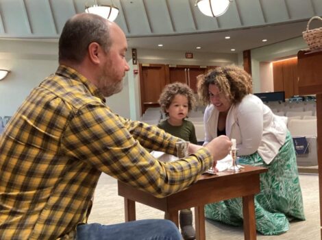 Man in yellow shirt works at a table with a toddler and a woman