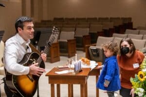 Rabbi Miller plays guitar while a young girl watches.