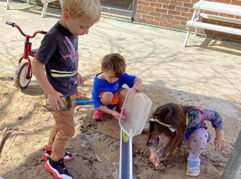 Children in the sandbox pour water down a trough