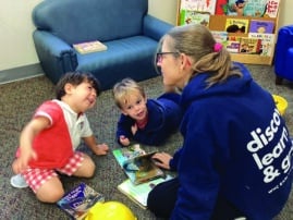 Teacher sits on floor with two young children