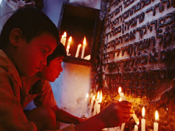 Two Indian boys light candles in front of a stone tablet with Hebrew writing on it